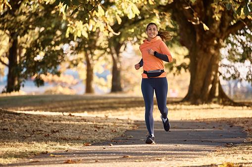 Young happy sportswoman running in the park during autumn day. Copy space.