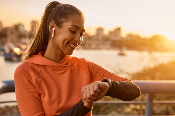 Happy sportswoman using fitness tracker while exercising at sunset. Happy athletic woman measuring her heart rate on smartwatch while after sports training at sunset. tracker stock pictures, royalty-free photos & images