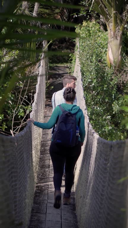 Couple of backpackers doing trekking and passing through an old hanging bridge among the forest.