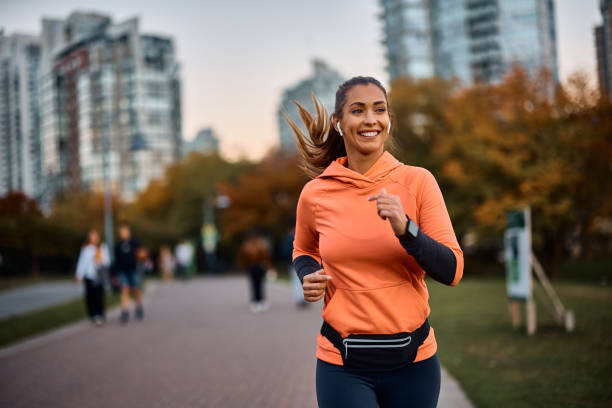 Happy sportswoman with earbuds running in the park. stock photo