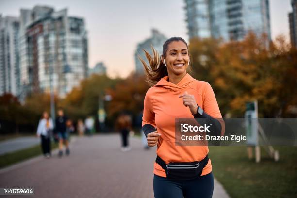 Happy Sportswoman With Earbuds Running In The Park Stock Photo - Download Image Now