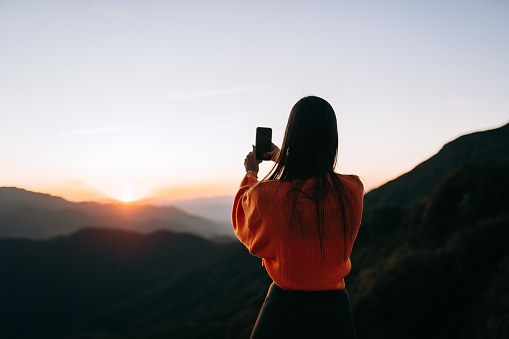 Woman taking picture of sunset on the mountain