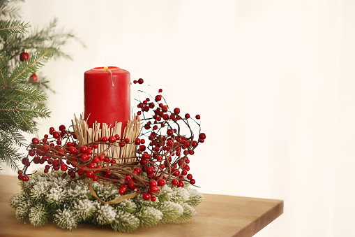 Red burning candle with christmas decoration, fir tree, in front of a white wall generous copy space