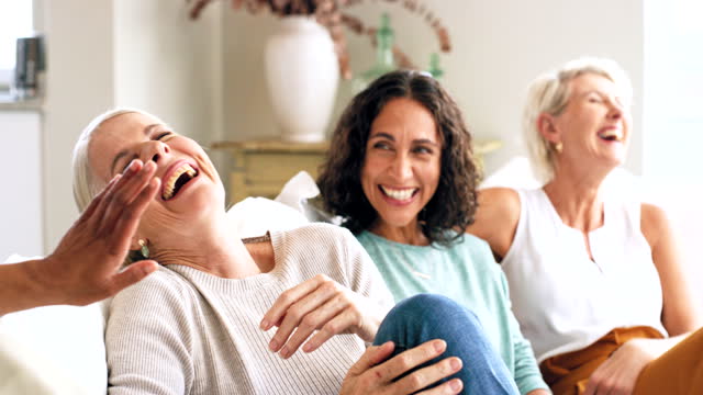 Senior women, friends and reunion at home talking, happy and together for quality time, communication and bonding on living room couch. Females laughing about comic conversation in retirement home