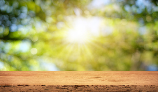 Empty wooden table are placed outdoors on green bokeh from natural leaves and sunlight. Counter display concept