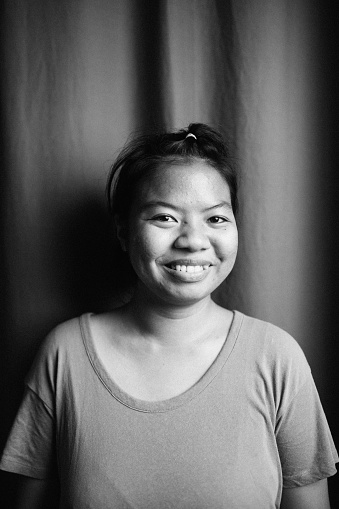A natural portrait of a Thai women standing in front of a curtain smiling from ear to ear
