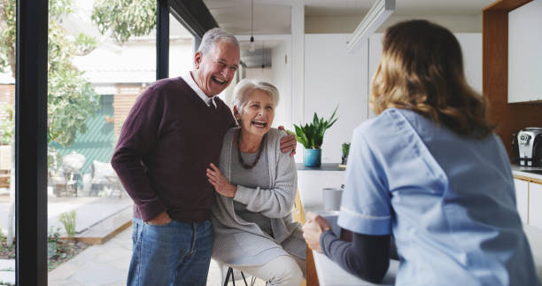 Couple, nurse and assisted living with a senior man, woman and caregiver laughing in a retirement home kitchen. Medical, healthcare and fun with an elderly male, female and carer joking in a house stock photo