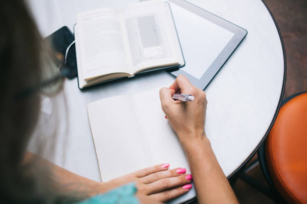 istock Cropped image of female student writing memo notes in textbook during information learning from literature book, selective focus on education equipment for exam preparation at table desktop 1441795257
