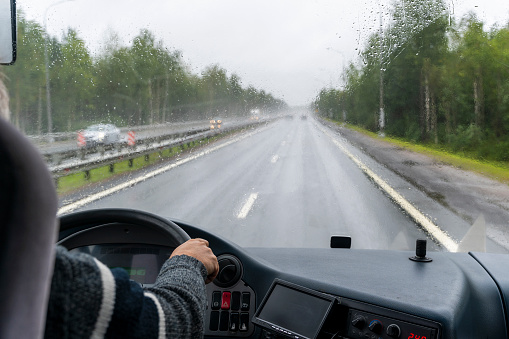 view through the windshield of a tourist bus moving along the highway during the rain. the driver is driving a tourist bus. road. driver holds on to the steering wheel