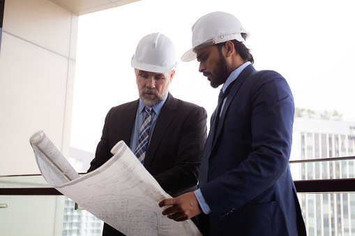 Senior architect inspector check blueprint and structure with contractor man and talking together at office, executive and supervisor or engineer planning project, industry and construction concept.