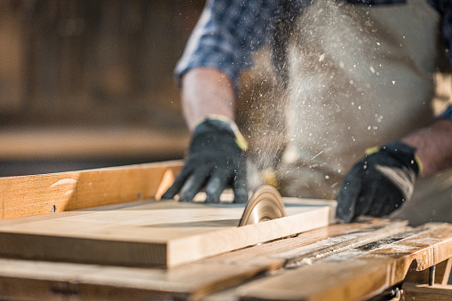 Close-up view of saw blade of electric circular saw cutting off thin stripe of material. Wood material processing in carpentry, handmade craftwork products.