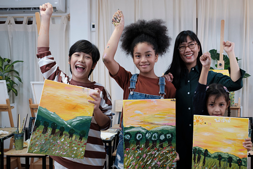 Group of art people in classroom studio, a teacher and student kids proud show painting work, an acrylic color picture on canvas, creative learning with talents skill at elementary school education.
