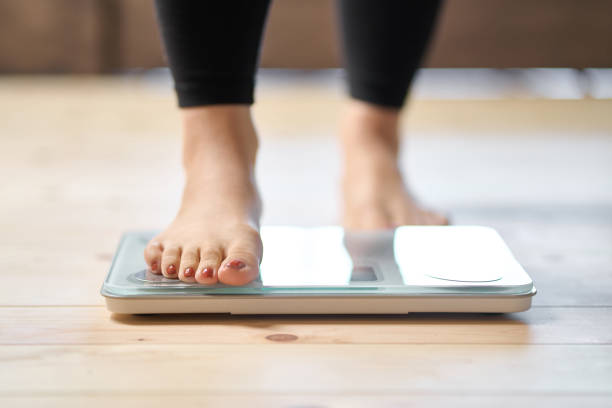 pieds d’une femme asiatique sur une balance de poids - régimes photos et images de collection