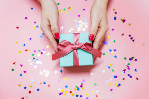 istock Female hands holding a gift box on pink background, top view 1441825070