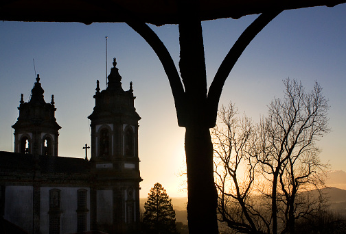 Church of Bom Jesus do Monte in Braga, Portugal, at dusk. Bell towers and bare trees back lit, sunset in the background.