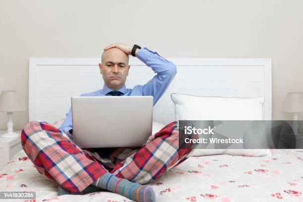Man Working With A Laptop On A Bed Dressed In A Shirt And Tie With A Worried Expression Stock Photo - Download Image Now