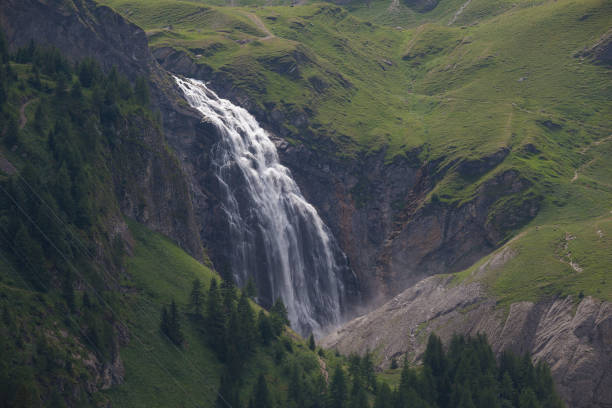 A dramatic waterfall is seen high up in the Jungfrau region of the Swiss Alps. A long exposure blurs the motion of the water.