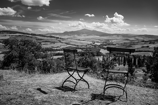 A grayscale shot of two metal chairs on the edge of a hill overlooking a landscape view