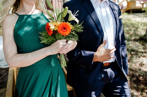 A closeup shot of a bridesmaid holding a colorful flowers bouquet walking on the aisle with a best man on a beautiful sunny day