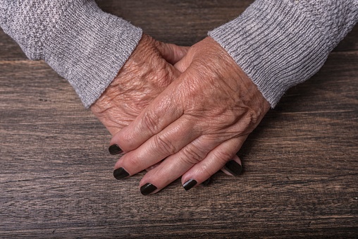 Hands of an old woman resting on a wooden table.