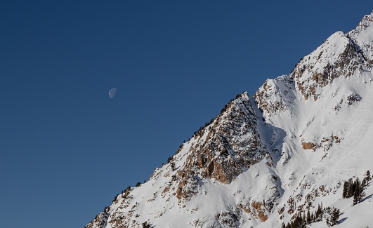 A beautiful view of the Moon setting over the Wasatch Mountains on a sunny day in Utah, United States
