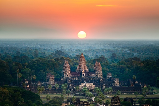 A bird's eye view of the Angkor Wat temple surrounded by greenery at sunset in Cambodia