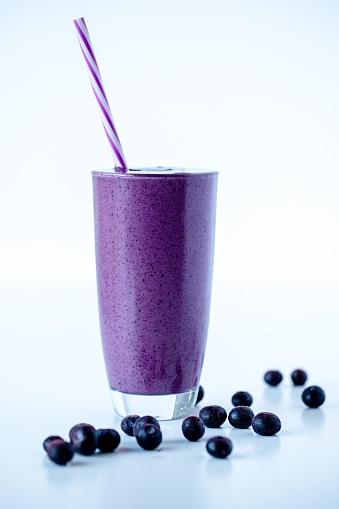 a Vertical shot of a blueberry milkshake in a  glass mug on white surface