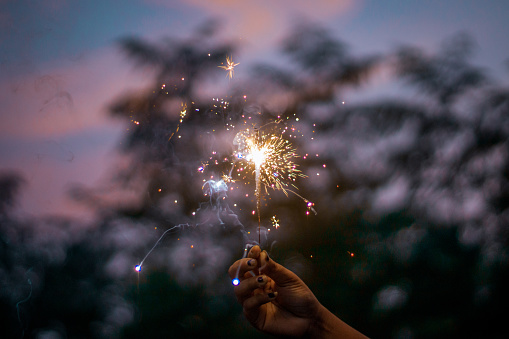 A sparkler in a female hand in the blurred natural background