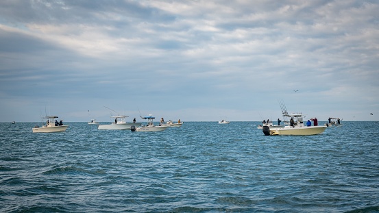 Harkers Island, United States – October 20, 2022: A group of people on small boats voyaging and fishing in the blue sea under cloudy sky