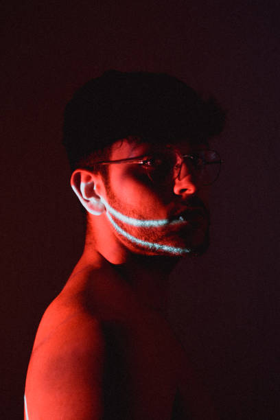 istock Young Hispanic artistic man with glasses posing in a dark room with a projector light on his face 1441837217