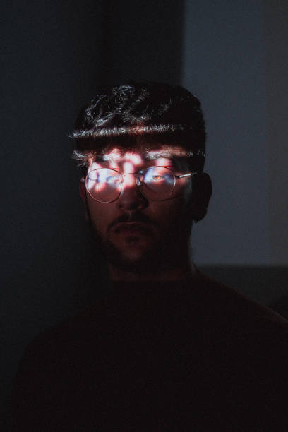 istock Young Hispanic artistic man with glasses posing in a dark room with projector light on his eyes 1441837241