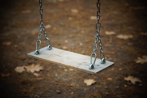 The high-angle shot of an empty simple wooden swing adjusted with chains on an autumn day