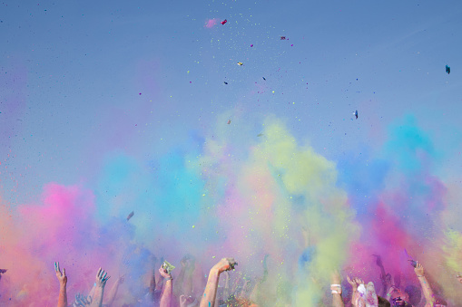 crowed of people with hands in the air and colorful powder in daytime blue skies