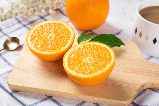 A closeup of fresh orange slices on a chopping board with a cup of coffee and whole orange beside it