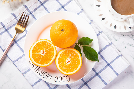 A top view of fresh oranges on a plate with a cup of coffee on the table