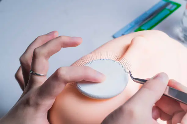 Photo of Female hand putting false eyelashes on a Mannequin face