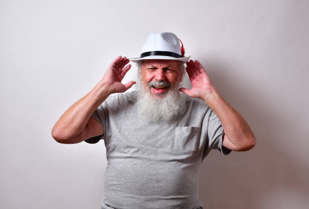 Old American male with a long white beard cupping his ears for better hearing An old American male with a long white beard cupping his ears for better hearing old man cupping his ear to hear something stock pictures, royalty-free photos & images