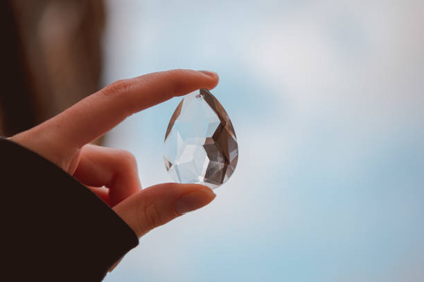 istock Teardrop-shaped crystal in a female hand in the light blue background 1441841051