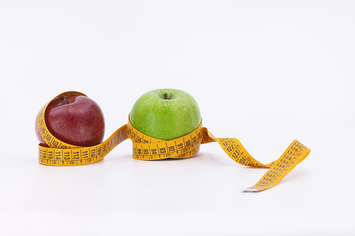 Green apple and red apple with measuring tape on white background