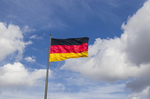 A pole with a waving German flag on the blue cloudy sky background