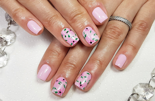 A closeup of a beautiful professional modern gel manicure in pink color with floral pattern