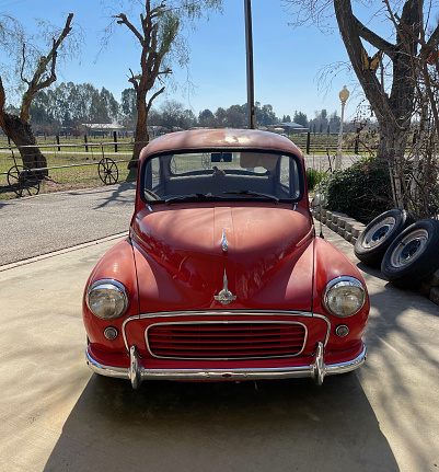 Fresno, United States – February 18, 2021: A photo of a front view of a really rare small British Minor 1000 Classic Car parked outside on driveway with a blue sky & trees in the background