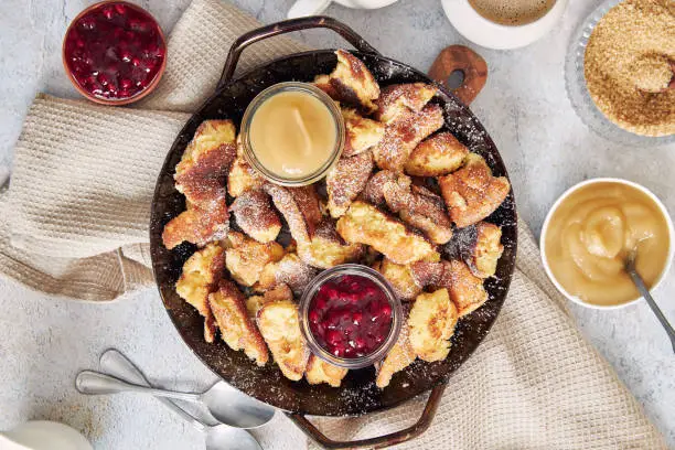 A top view of kaiserschmarrn with torn pancakes, cranberries jam, and apple puree on a table