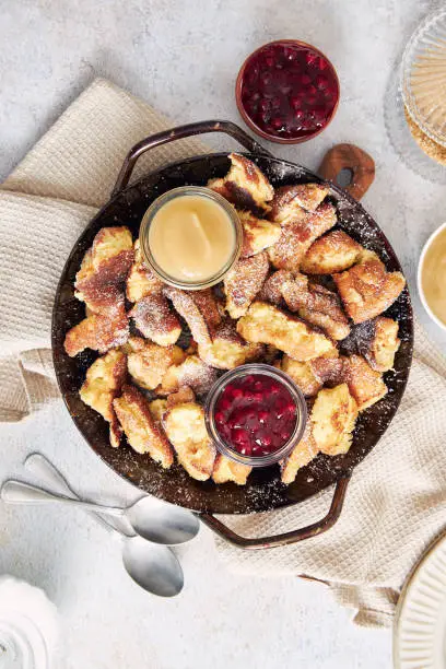 A top view of kaiserschmarrn with torn pancakes, cranberries jam, and apple puree on a table