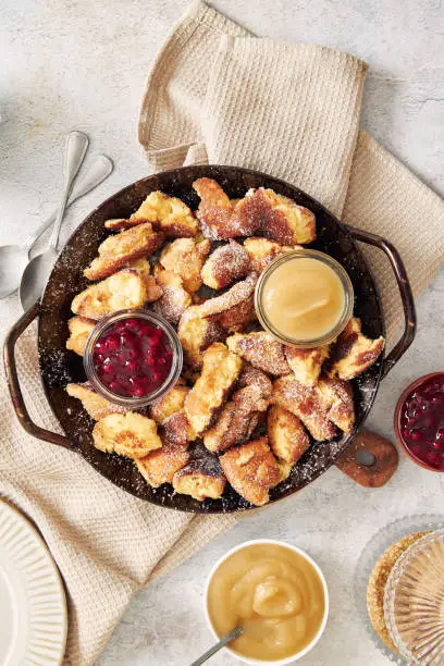 A vertical shot of kaiserschmarrn with torn pancakes, cranberries jam, and apple puree on a table