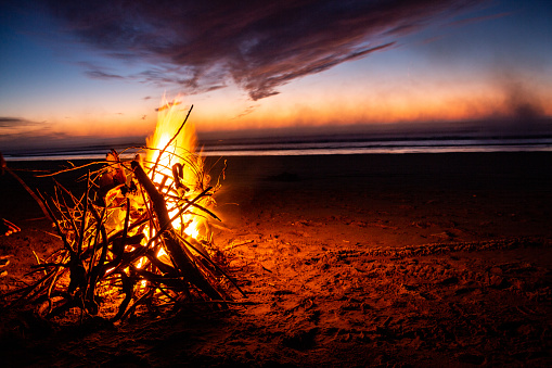 A bright bonfire burning at the beach in the evening; the vibrant sunset sky in the background