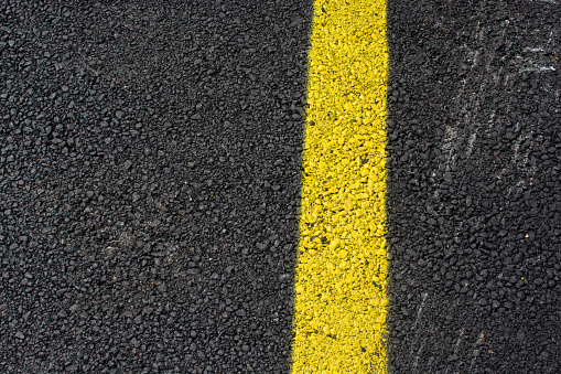 A high angle shot of a yellow line painted on the asphalt