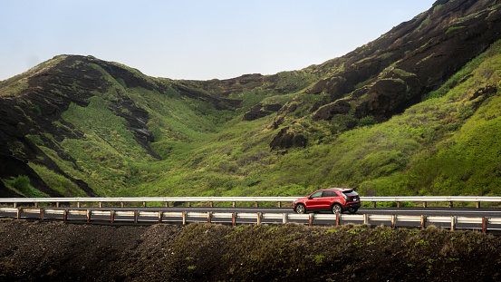 A red-colored SUV car driving on a road in a beautiful field captured during the daytime