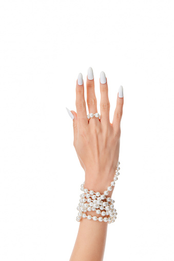 A female hand with long white nails wearing a pearl bracelet isolated on a white background