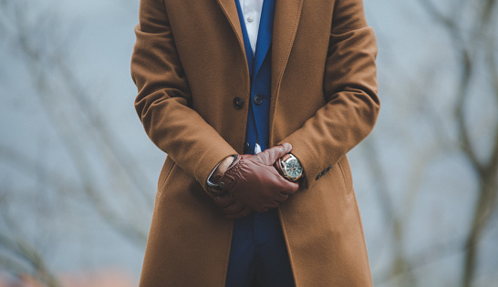 A selective focus of an elegant man wearing a classic brown coat with leather  gloves